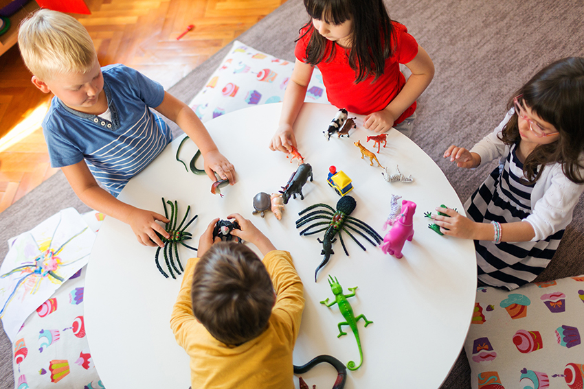 Four children playing with plastic animal toys at a low round table.