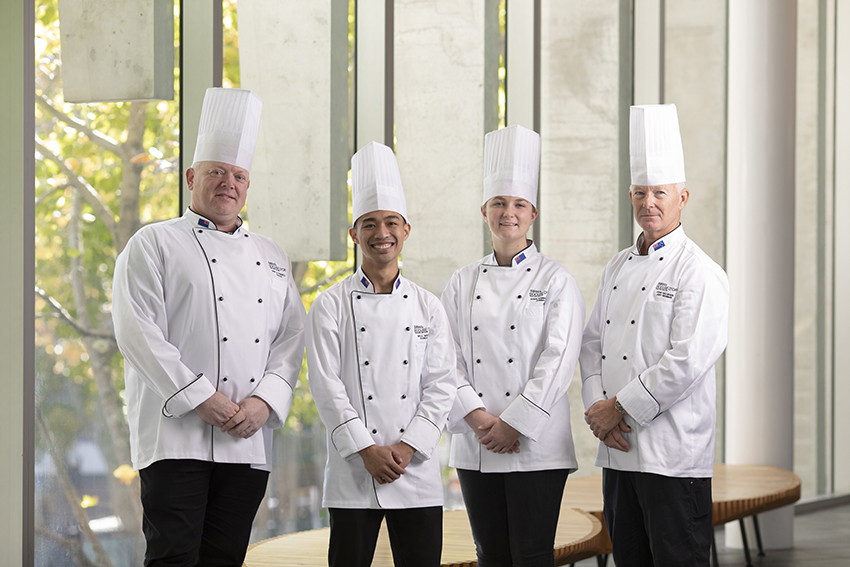 Four members of the team standing in chef whites and hats smiling and looking at the camera.
