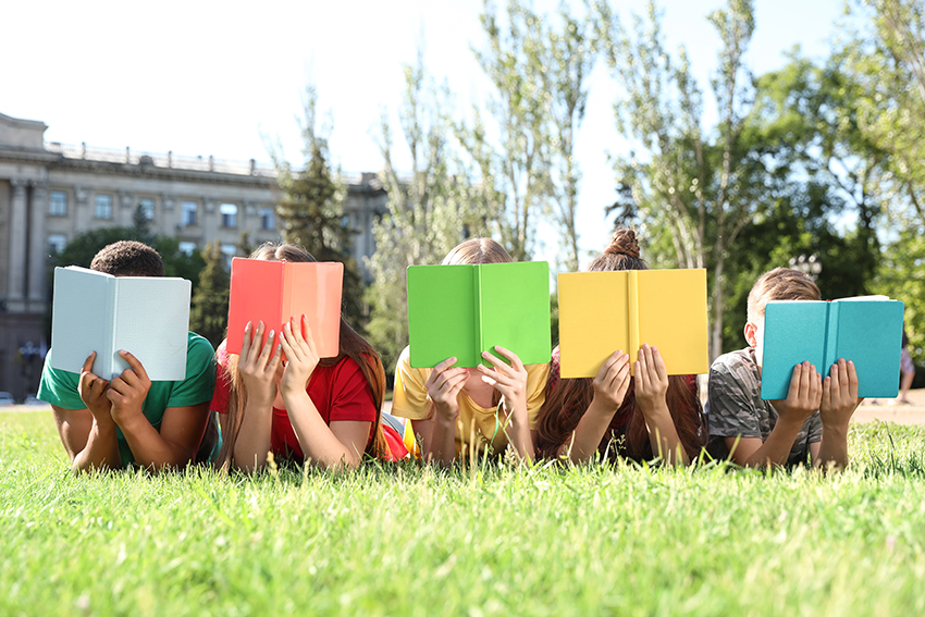 children lying on the grass, heads in books