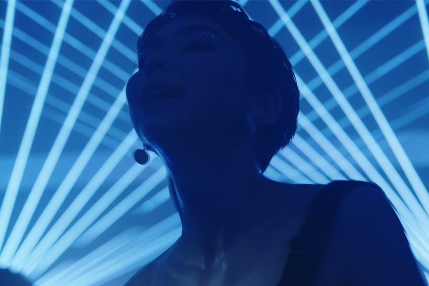 Woman with short hair in a blurred shadow with blue laser lights in beaming in the background.