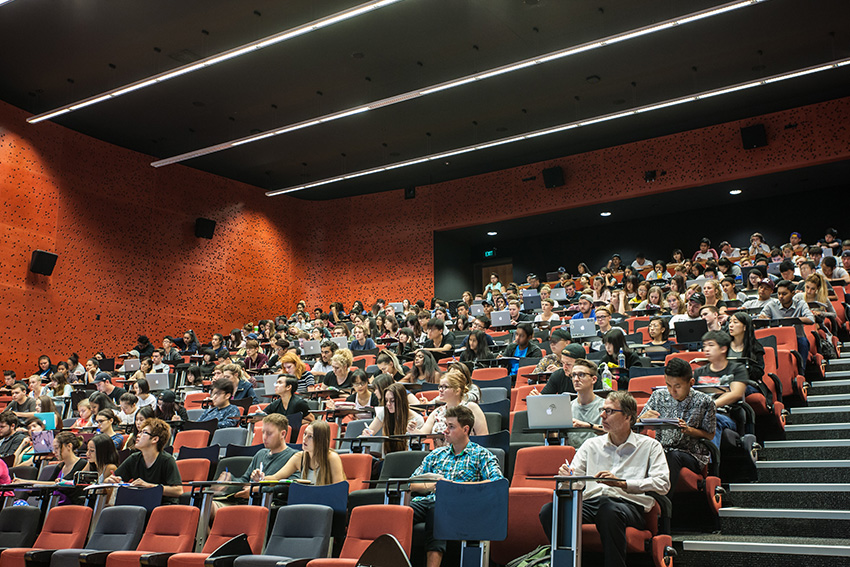 AUT students in a WG lecture theatre. Some students are writing down notes, some are typing on their laptops and some are looking at the projection.